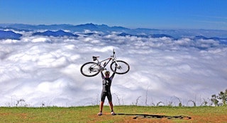 This picture shows a man with his bicycle in the top of a mountain